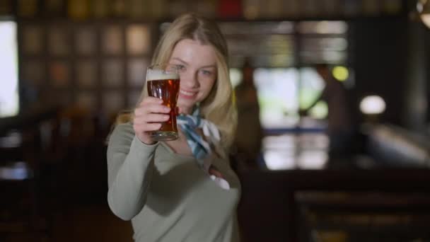 Jovem feliz brindar esticando copo de cerveja para câmera sorrindo em pé no pub dentro de casa. Foco cremalheira de sorrir face a pint de cerveja e volta. Conceito de lazer e estilo de vida de fim de semana. — Vídeo de Stock