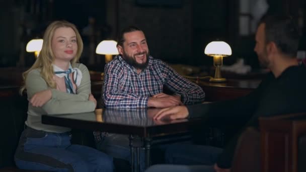 Skrattande skäggig man som pratar med vänner som sitter på restaurang och väntar på order. Porträtt av positiva glada kaukasiska män och kvinnor vilar njuter av mötet inomhus i caféet. Vänskap och fritid. — Stockvideo