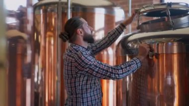 Bira fabrikasındaki büyük bira tankını tamir eden konsantre mühendis. Odaklanmış beyaz erkek uzmanın, kırık ekipmanları içeride tamir ederken yan görünüm portresi. Alkol üretimi ve bakımı.