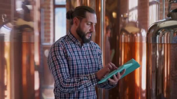 Homme confiant debout dans la brasserie avec tablette vérifier les commandes en ligne pour la bière de haute qualité. Portrait d'un beau brasseur barbu caucasien gérant des affaires électroniques produisant de l'alcool. Mode de vie et affaires. — Video