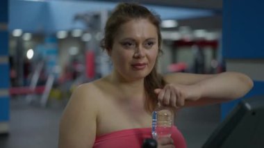Spor salonundaki idmandan sonra su içen iri yarı, beyaz bir kadın. Kapalı alanda antrenman yapan ısrarcı genç sporcunun portresi. Spor ve motivasyon kavramı.