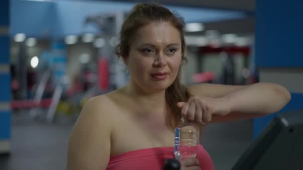 Plus storlek vit kvinna dricksvatten uppfriskande efter träning i gym. Porträtt av motiverade uthålliga unga idrottskvinna träning inomhus. Idrott och motivation. — Stockvideo