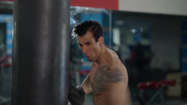 Spor salonunda çıplak vücut boksu yapan kendinden emin Ortadoğulu bir adam. Yakışıklı, formda boksör portresi. Kum torbasına vuruyor. Spor ve dövüş sanatları konsepti. — Stok video