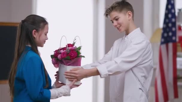 Glimlachende jongen in doktersjurk gefeliciteerd meisje met Womens Day verrassende zus met mand van bloemen. Dankbare blanke broer en zus knuffelende broer aan het praten. Familie eenheid en vakantie viering. — Stockvideo