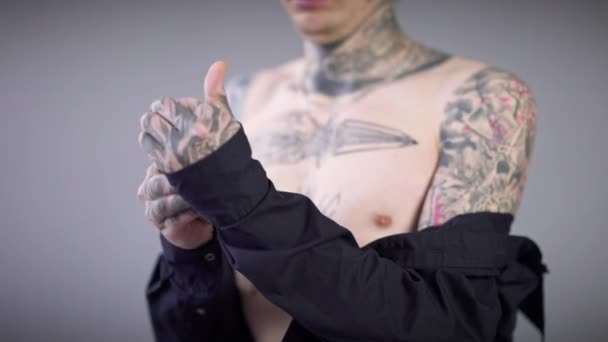 Nerozpoznatelný potetovaný muž se svléká a odchází. Mladý běloch s tetováním na rukou, trupu a krku, svléká si černou košili a odchází na šedém pozadí. Koncept rozmanitosti a stylu. — Stock video