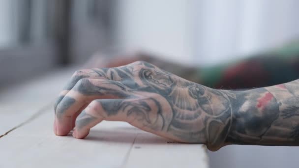 Vista lateral de cerca manos tatuadas masculinas con los dedos golpeando en el alféizar de la ventana. irreconocible ansioso caucásico milenial chico de pie en la ventana en el interior pensando. — Vídeo de stock