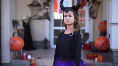 Cadılar Bayramı kostümü giymiş güzel bir kızın portresi dışarıda durmuş, dekore edilmiş evi korkutan bir çocuğun dışarı çıkmasını bekliyor. Neşeli Kafkasyalı çocuklar Cadılar Bayramı 'nda dışarıda eğleniyorlar..