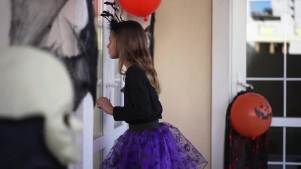 Портрет симпатичной белой девушки в костюме, стоящей у дома, украшенного на Хэллоуин, заглядывающей внутрь. Симпатичный ребенок ищет фокус или угощение на отдыхе. Традиционная концепция праздника. — стоковое видео
