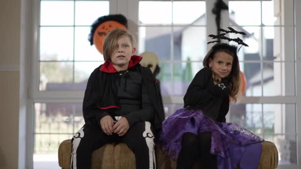 Vorderansicht zwei Kinder, die sich drinnen Horrorfilme über das Gruseln an Halloween ansehen. Niedlichen kaukasischen verängstigten Jungen und Mädchen sitzen im Wohnzimmer im Urlaub mit verängstigten Gesichtsausdruck. Zeitlupe. — Stockvideo