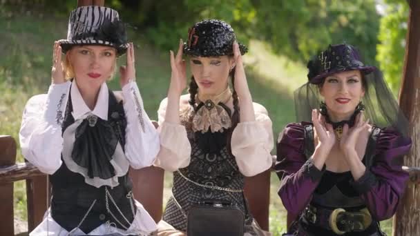 Средний снимок портрета трех великолепных уверенных в себе кавказских женщин в стимпанк-костюме, позирующих на улице под солнцем. Красивые дамы, смотрящие в камеру и улыбающиеся шляпы. Футуристический стиль Cosplay. — стоковое видео