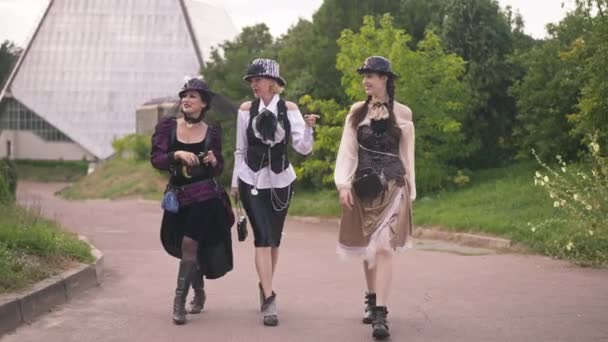 Wide sköt tre självsäkra glada vackra kvinnor i steampunk outfit promenader i slow motion utomhus prata och skratta. Glada smala vackra vita damer promenader på solig dag. Stil koncept. — Stockvideo