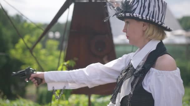 Side view woman on the right aiming shooting with gun making scared facial expression throwing away weapon. Frightened Caucasian lady in steampunk costume on Halloween outdoors. — Stock Video