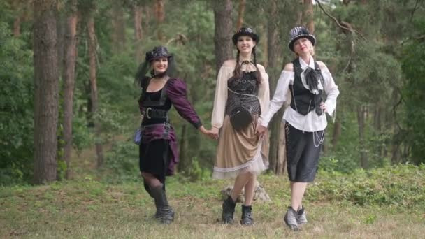 Szeroki strzał kobiet w stroju steampunk pozowanie w lesie na zewnątrz Halloween. Szczęśliwy uroczy pewny siebie piękne białe panie patrząc na aparat chwaląc się popisując się w lesie na wakacje. Zwolniony ruch. — Wideo stockowe