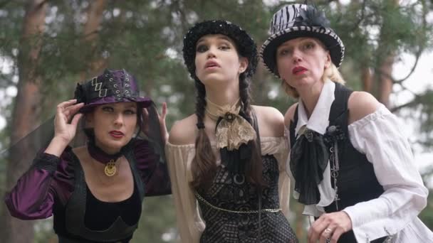 Three concentrated women looking at camera posing in steampunk Halloween costumes outdoors in forest. Caucasian beautiful slim ladies in woods with curios facial expression. Slow motion. — Stock Video