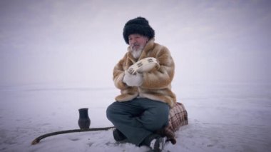 Donmuş kutup okyanusunda oturan tef çalan konsantre şaman. Geniş açılı, kendinden emin, yaşlı yerli bir adam, açık havada, pitoresk manzarada dua ediyor. Maneviyat kavramı.