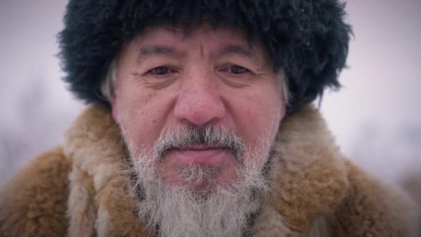 Cabeza triste solitario anciano indígena en sombrero y abrigo de piel al aire libre. Retrato de cerca del desesperado chico asiático en el frío día de invierno pensando y mirando a la cámara. Movimiento lento. — Vídeo de stock