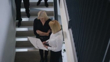 Yüksek açı, profesyonel kadınların evrak işlerini analiz etmesi ve alt katta ve üst katta iş arkadaşlarını selamlayan erkeklerle konuşması. İş ve yaşam tarzı.