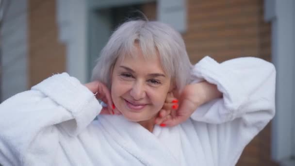 Tevreden volwassen vrouw kijkt naar camera stretching en glimlachen buiten staan op de achtertuin of voortuin. Close-up portret gelukkig mooi blank dame poseren in de ochtend. — Stockvideo