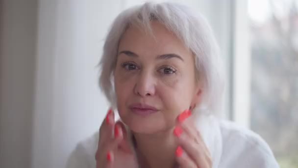 Front view face of mature woman examining wrinkles looking at camera. Mirror POV of worried Caucasian lady indoors at home in the morning. Aging and femininity concept. — Stock Video