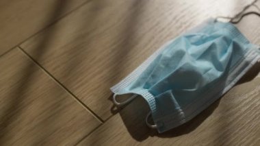 Üst Manzara Covid-19 yüz maskesi ahşap masanın üzerinde güneş ışınlarıyla soldan sağa hareket ediyor. Kapalı alanda güneş ışığıyla kaplanmış koronavirüs yüzü. Küresel pandemik kilitleme kavramı.