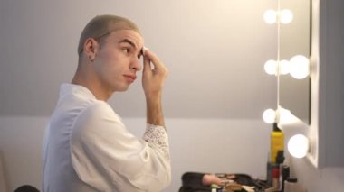 Kendine güvenen LGBT adamı, kaş temizleyicisi, pamuk yastığı yavaş çekimde ovalıyor. Sabahları evde makyaj yapan beyaz ırktan olmayan birinin portresi..