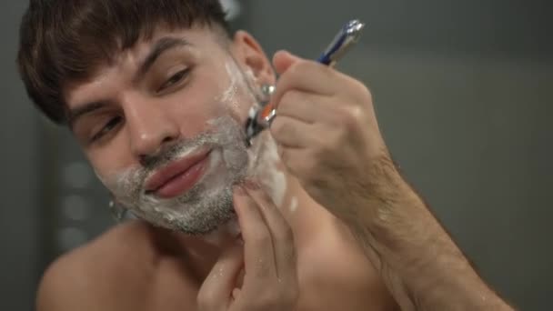 Zblízka pohled muž holení tvář úsměv ve zpomaleném filmu. Portrét sebevědomého bělocha, který se doma v koupelně holí strništěm. Rutinní a hygienický koncept. — Stock video