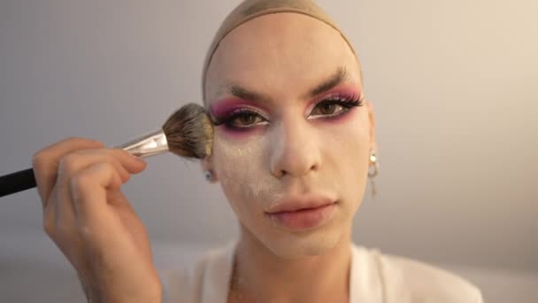 Gros plan visage de travesti homme appliquant de la poudre visage au ralenti posant à l'intérieur. Prise de vue de la personne LGBT fluide de genre caucasien faisant maquillage regardant la caméra. Beauté et identité de genre. — Video