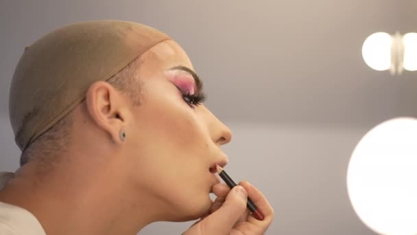 Side view extravagant Caucasian LGBT man with makeup on eyes applying lip pencil in slow motion. Close-up face of concentrated young non-binary person doing makeup. Confidence and diversity. — Stock Video