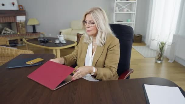 Portret poważnej psychologi otwierającej laptopa siedzącej przy stole w pomieszczeniu. Skoncentrowana biała kobieta w okularach zaczyna rano pracować w biurze.. — Wideo stockowe