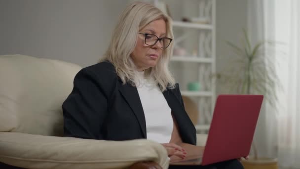 Porträt eines konzentrierten Psychologen, der mit Laptop auf einem Sessel sitzt und die Uhrzeit überwacht. Medium erschossen schöne kaukasische Frau mit Brille wartet auf Patienten. Expertise und psychologisches Konzept. — Stockvideo