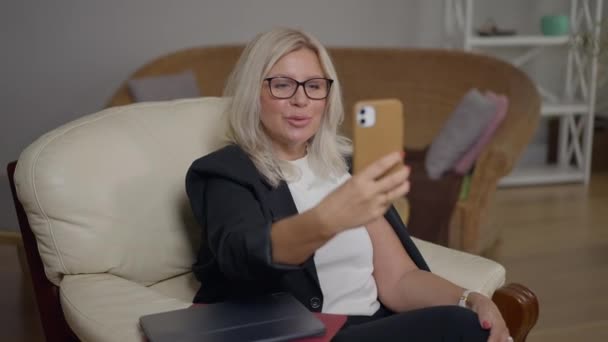 아름다운 전문 심리학자가 스마트폰으로 비디오 채팅을 하고 아늑 한 안락의자에 앉아서 웃고 이야기하는 것이죠. 온라인상에서 상담하는 전문가 코카서스 지적 전문 여성의 모습. — 비디오
