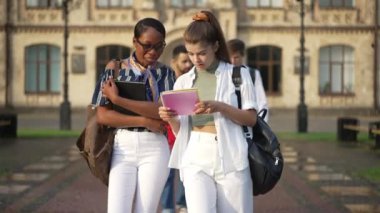 Ön bakış açısı pozitif Afrikalı Amerikalı ve beyaz kadınların güneşli bir günde kampüste yürüyüp konferansları tartışmalarına odaklandı. Erkekler arka planda gezinip konuşuyorlar. Üniversite yaşam tarzı ve eğitimi.