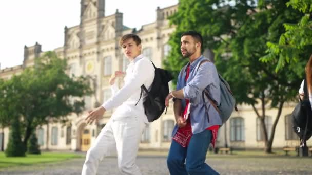 Χαρούμενη ενθουσιασμένοι άνδρες φοιτητές πανεπιστημίου χορεύουν στην αυλή του πανεπιστημίου διασκεδάζοντας με τις γυναίκες groupmates περνώντας στην πανεπιστημιούπολη στο παρασκήνιο. Χαλαρός αυτοπεποίθηση ευτυχισμένοι άνδρες απολαμβάνοντας ηλιόλουστη μέρα σε εξωτερικούς χώρους. — Αρχείο Βίντεο