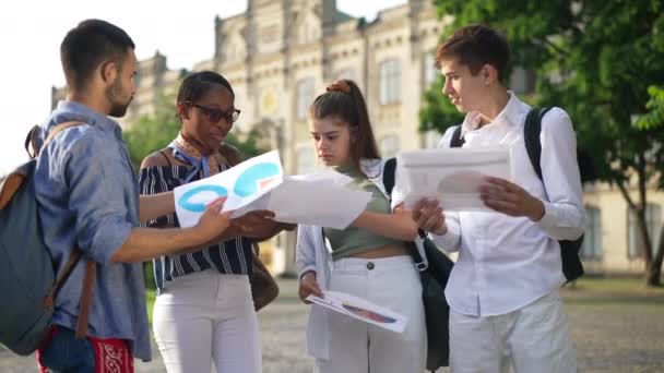 Zaneprázdnění mladí studenti mluví o papírování diskutovat o skupinovém projektu venku za slunečného dne. Inteligentní multietničtí muži a ženy plánující univerzitní kampus. Vzdělávání a inteligence. — Stock video