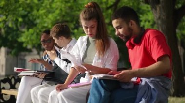 Yandan bakıldığında, beyaz bir kadın, arka planda konuşan, arka planda oturan, Orta Doğulu bir adamla çalışmaları tartışıyor. Dışarıda güneş ışığında yoğunlaşmış çok ırklı öğrenciler.