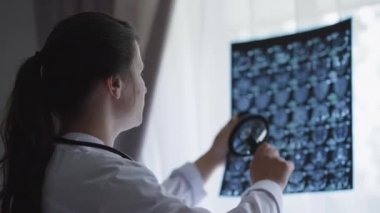 Zeki Kafkas genç doktor büyüteçle beyin röntgenini analiz ediyor. Hastanede, pencerenin önünde duran Roentgen 'i inceleyen konsantre olmuş güzel esmer kadın..