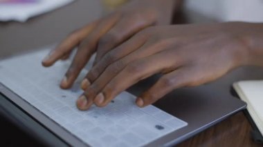 Kapalı mekanda dizüstü bilgisayarlı klavyeyle mesaj atan yakın plan erkek Afro-Amerikan elleri. İnternette mesaj yazan tanınmamış bir genç adam internette sörf yapıyor. Modern teknolojiler ve konsept.