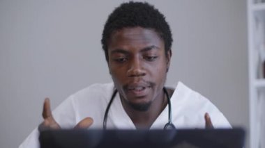 Yakın plan portre, ciddi zeki Afro-Amerikan doktor dizüstü bilgisayarda oturuyor içeride konuşuyor ve el kol hareketi yapıyor. Kendine güveni tam bir adam hastanede konferans düzenliyor. Tıp mesleği yaşam tarzı.
