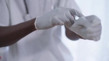 Yakın plan erkek Afro-Amerikan elleri cerrahi eldiven takıyor. Tanınmayan bir doktor hastanenin içinde ameliyata hazırlanıyor. Sağlık ve Tıp Konsepti.