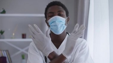 Ön manzara portresi. Covid maskeli ciddi bir Afrikalı Amerikalı doktor. Kameraya bakmadan el hareketi yapıyor. Profesyonel uzman genç adam Coronavirus salgını yüzünden hastanede poz veriyor..