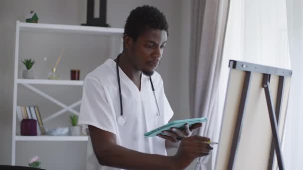 Μέτριο πυροβόλησε έξυπνος Αφροαμερικανός γιατρός στέκεται στο whiteboard με το γράψιμο tablet με δείκτη. Συγκεντρωμένος έξυπνος νέος που αναλύει τις παρενέργειες του εμβολιασμού και την αποτελεσματικότητα. — Αρχείο Βίντεο