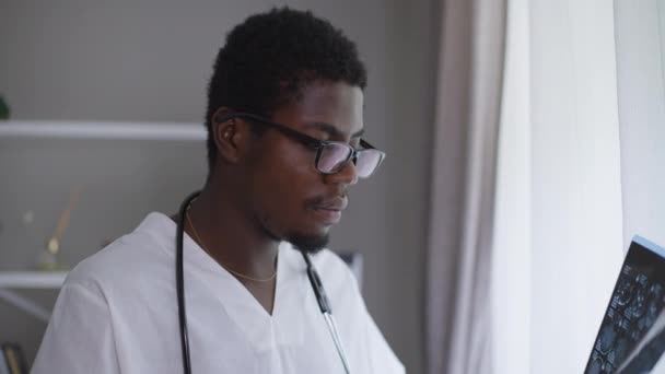 Мужчина, афро-американский невролог, анализирует рентгеновский вздох, снимающий очки. Вы не уверены, что доктор осматривает болезнь в больнице в помещении. Сомнения и медицинская концепция. — стоковое видео