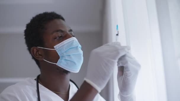 Close-up deskundige Afro-Amerikaanse arts op het gebied van coronavirus gezichtsmasker met spuit met Covid-19 vaccin. Serieuze man in het ziekenhuis die vaccineert bij een pandemie. Vax-concept. — Stockvideo