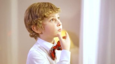 Noel arifesinde evde Noel Baba 'yı beklerken pencereden dışarı bakan sevimli çocuk. Yeni yılda gömlekli ve papyonlu sevimli beyaz çocuk portresi. Çocukluk kavramı.