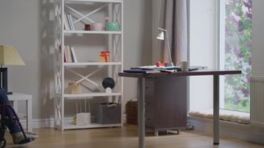 Geniş açılı ofis, engelli genç bir kadın tekerlekli sandalyeyle masa açma bilgisayarına doğru ağır çekimde dönüyor. İnternette çalışan ciddi bir Kafkas uzmanının portresi..