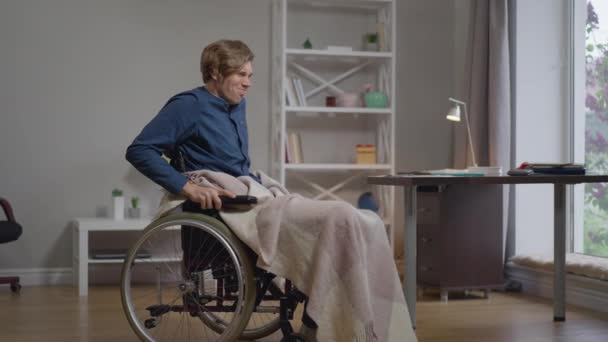 広いショットは、スローモーションで屋内の自宅で車椅子に立つしようとしている若い障害者の動機付け。白人の肖像は、病気から回復する努力をする自信を持った奇術師を鼓舞しました. — ストック動画