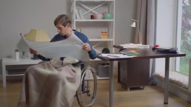 Genç yetenekli engelli erkek mimar yavaş çekimde planlarını inceliyor. İçerideki ofiste, tekerlekli sandalye planlama projesinde çalışan, konsantre olmuş, beyaz bir adamın portresi..