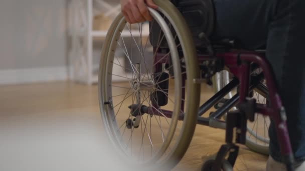 Unerkennbarer Rollstuhlfahrer fährt in Zeitlupe von Haus zu Haus. Junger Kaukasier gelähmt zu Hause im Wohnzimmer. Krankheits- und Behindertenkonzept. — Stockvideo