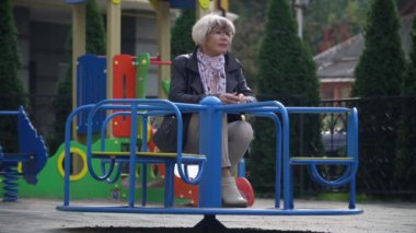 Geniş açılı, düşünceli, üzgün, yaşlı, güzel bir kadın dışarıda oyun parkında atlıkarıncada oturuyor. Kafkas ince, muhteşem, yalnız bir kadının portresi. Yaşlanma ve yaşam tarzı kavramı.
