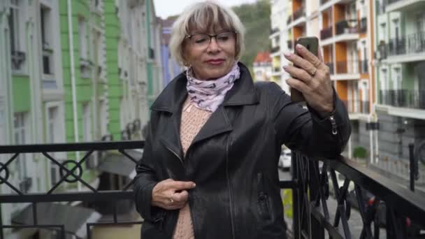 Encantador turista senior seguro de tomar selfie en el teléfono inteligente de pie en la calle de la ciudad al aire libre. Retrato de una hermosa mujer caucásica delgada disfrutando del turismo sonriendo. Estilo y confianza. — Vídeos de Stock